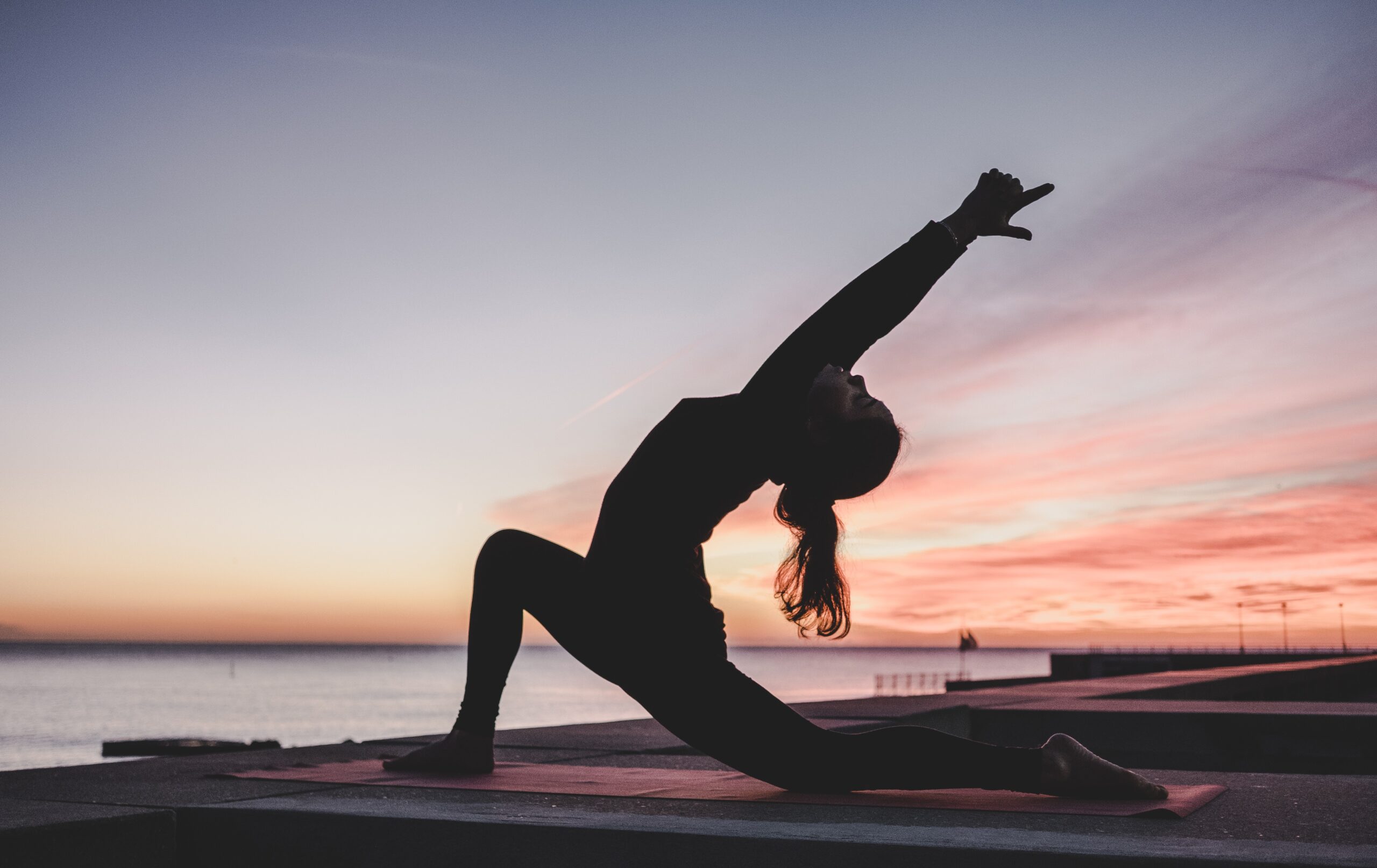Silhouette of woman doing yoga pose in front of purple and pink sunset.