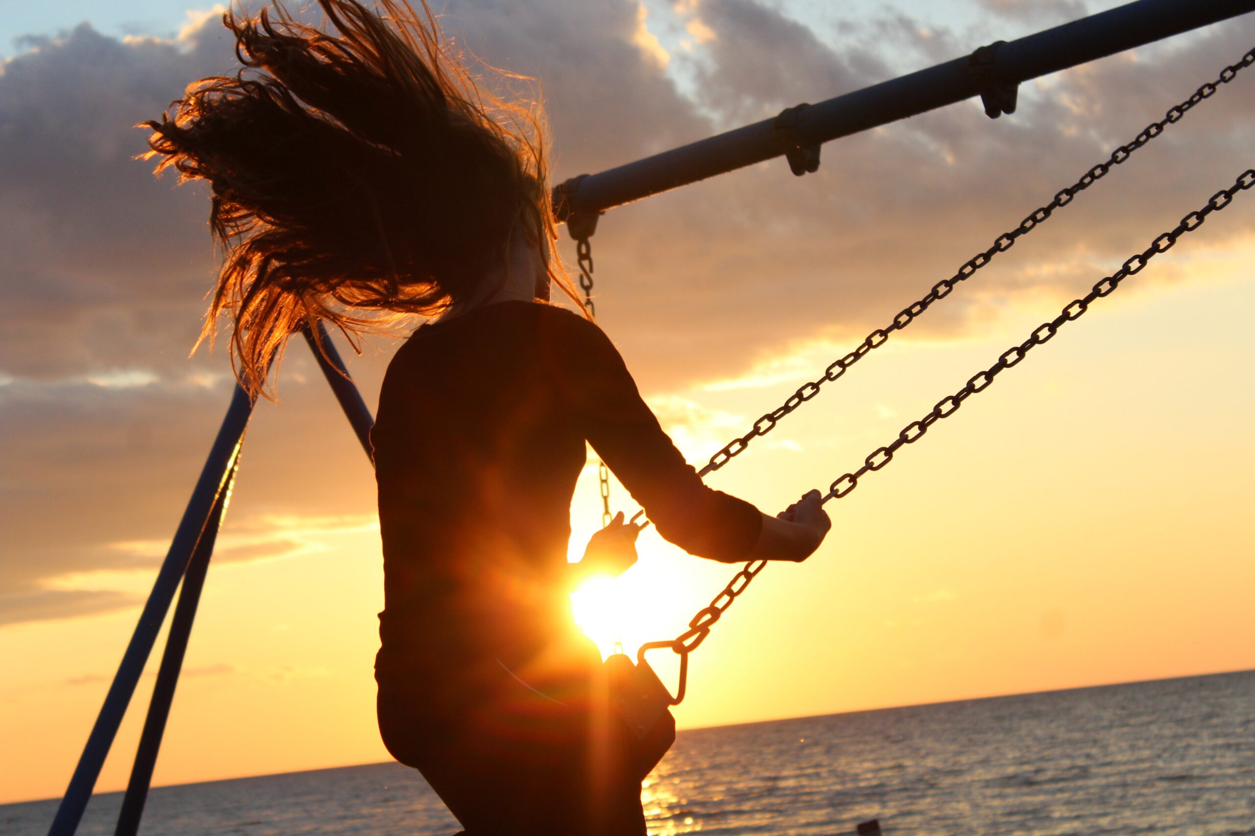 woman on swing, near sea, at sunset